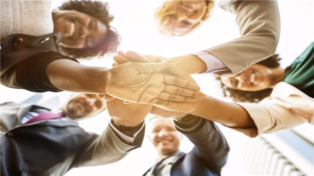 Group of people standing in a circle with their hands meeting in the middle